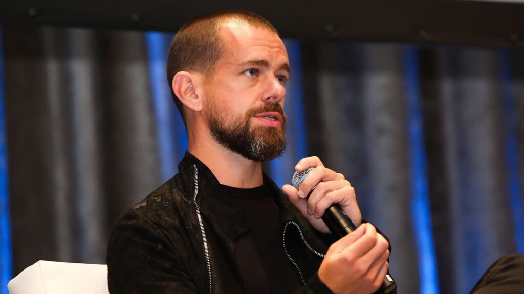 Man with a beard holding a microphone and speaking on stage during an event
