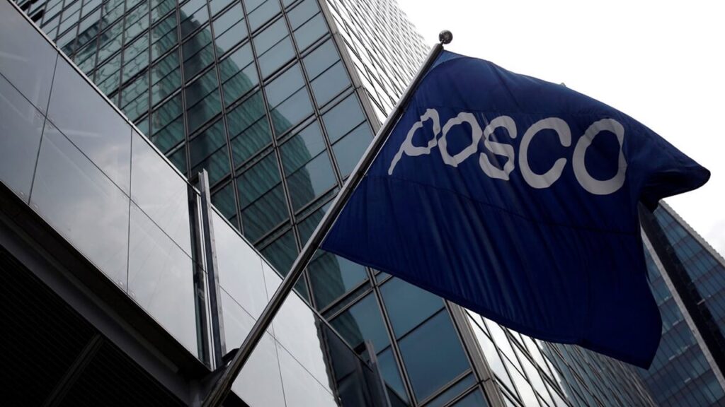Blue flag with the POSCO logo fluttering in front of a glass office building.