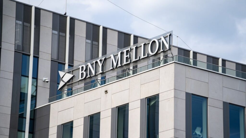 Modern office building with a large BNY Mellon sign on the rooftop, a glass railing nearby.
