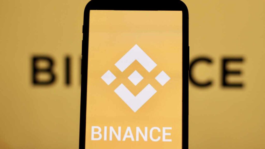 Phone screen showing the Binance logo on a yellow background, branding for the cryptocurrency exchange.