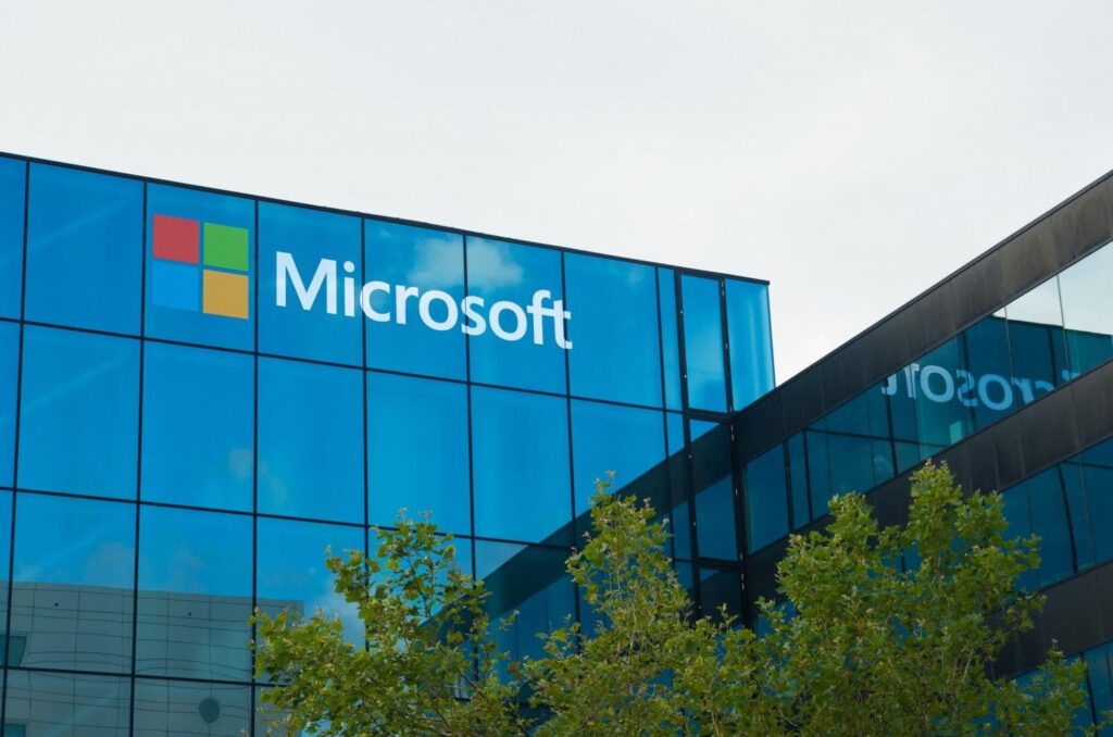 no_translation_5049_ffhaj7cer7v0iim75vzkfy4c_no_translation_translation - Crypto and Coin Microsoft logo displayed on a blue glass office building with green trees in the foreground,