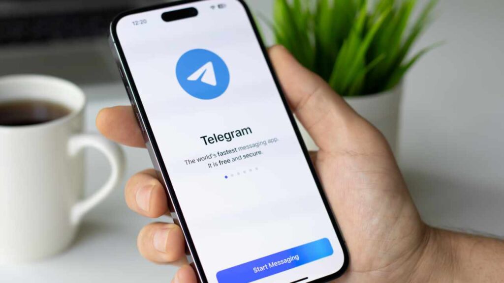 Hand holding a smartphone displaying the Telegram welcome screen with a 'Start Messaging' button.
